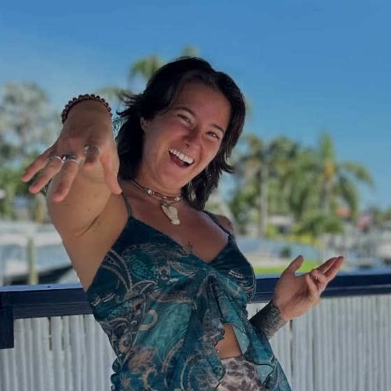 Megan Nardi laughing, reaching her hands toward the camera, palm trees behind her.