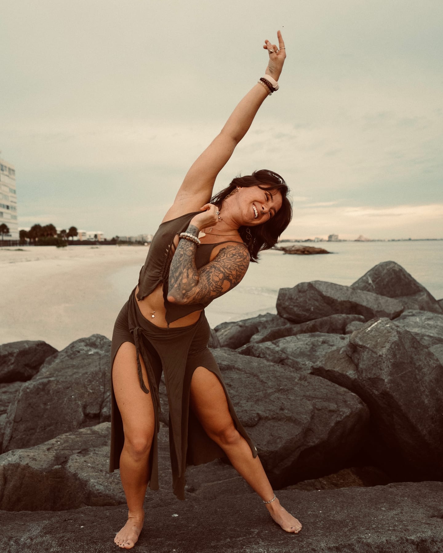 Megan Nardi laughing mid-movement on the rocks by the water, one arm reaching skyward